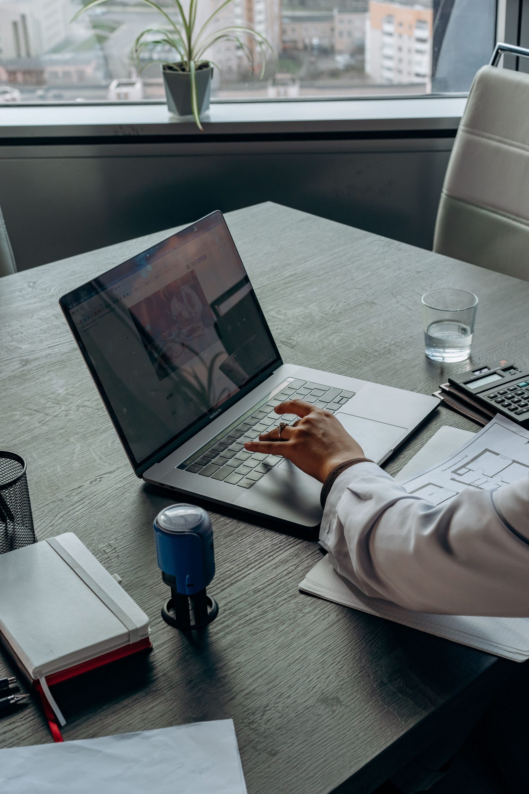 An office scene showing a person working on a laptop with papers on a wooden table.